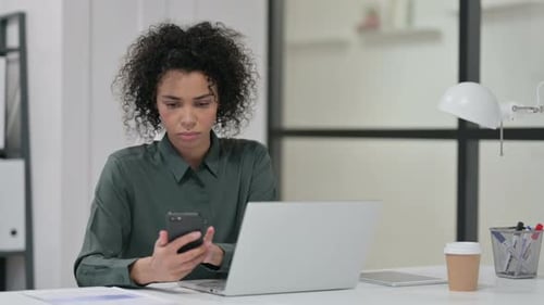 Woman Using Smartphone While Working on Laptop