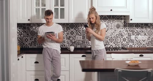 Couple Using Devices in Modern White Kitchen
