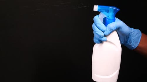 Hand Sprays Bottle of Cleaner Against Black Background
