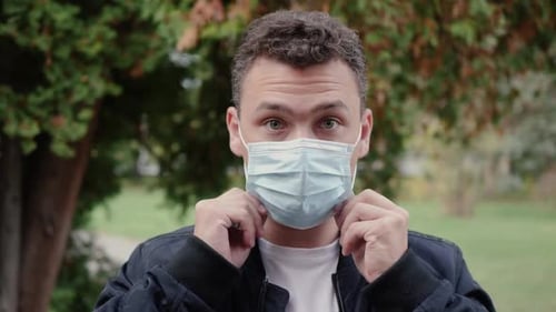 Man Puts on Blue Surgical Mask Outdoors