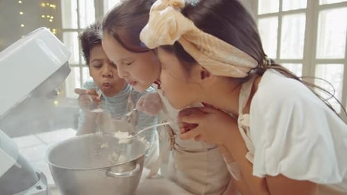 Fröhliche Kinder blasen bei Cooking Masterclass Mehl aus Löffeln