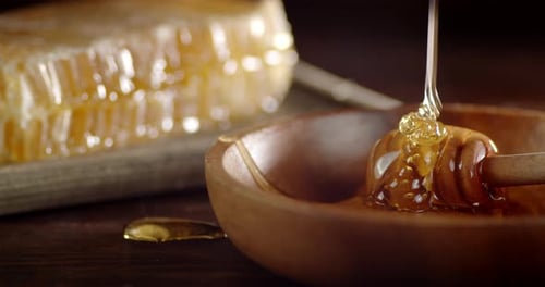 A Stream of Honey Flows Into a Wooden Plate on the Table.