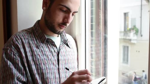 Young Adult Writing in Notebook by Window