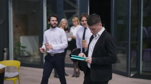 Thoughtful Young Caucasian Male Employee Standing on Sunny Office Terrace with Tablet Planning