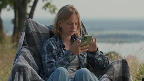 Woman Uses Phone While Relaxing Outside in Nature