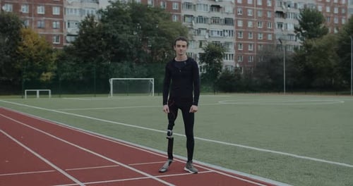 Positive Disabled Man with Prosthetic Running Blades Standing at Sports Field