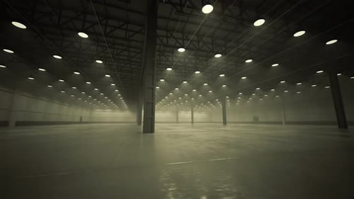 Interior of large, empty industrial warehouse with concrete floor and lamps.