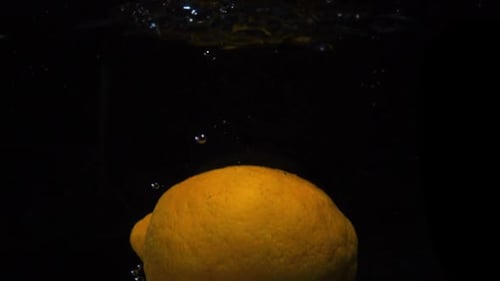 Le citron jaune tombe dans l'eau sur fond noir. Prise de vue macro au Ralenti. Vidéo culinaire : Citron