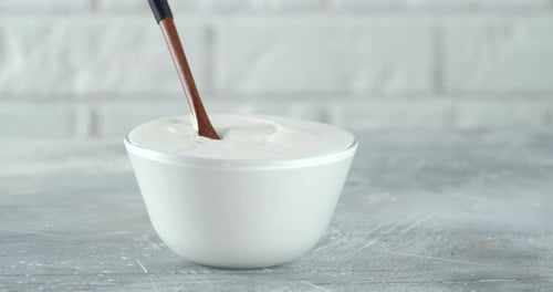 Sour Cream in a Bowl with a Spoon Slowly Rotates.