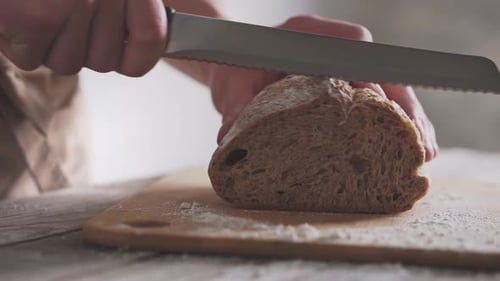 Person Slicing Fresh Bread Loaf on Cutting Board