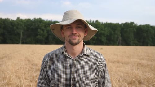 Close Up of Happy Smiling Farmer in Hat Looking Into Camera Against the Blurred Background of Wheat