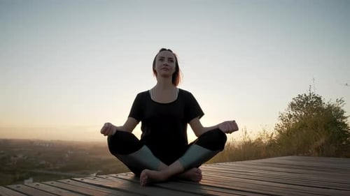Woman Meditates at Sunrise Overlooking City