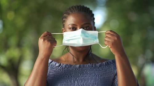 Front View Portrait Serious African American Woman Putting on Coronavirus Face Mask Looking at