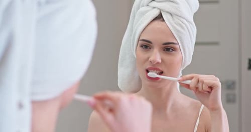 Woman Brushing Teeth in Bathroom Mirror