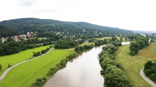 Aerial Drone Shot a Large River Runs Through a Hilly Rural Area with Villages on a Sunny Day