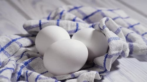 Tres huevos de gallina crudos sobre la mesa, chupito giratorio, blanco, huevos crudos frescos en un trozo de tela
