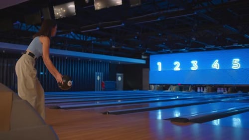 A Brunette Woman in Bowling Throws a Ball in Slow Motion and Knocks Down Skittles