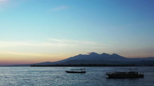 Peaceful seascape after sunset with colorful sky reflecting on dark sea surface, boats anchoring on