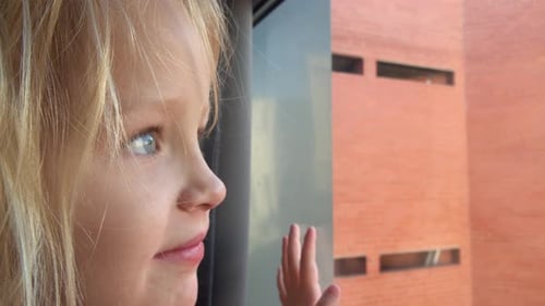 Cheerful and Curious Little Girl Looking Outside Through the Window