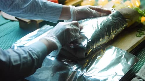 Gloved Hands Wrapping a Sandwich in Foil