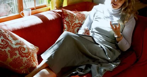 Woman Relaxing on Sofa with Phone and Notebook