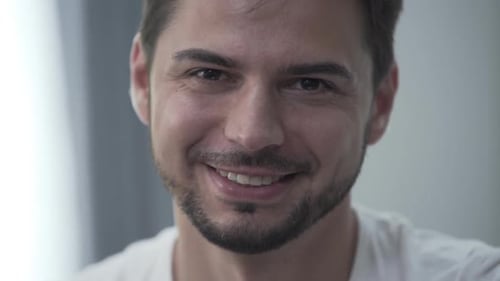 Porträt eines gutaussehenden lächelnden Mannes in weißem T-Shirt, der zu Hause sitzt und lächelt