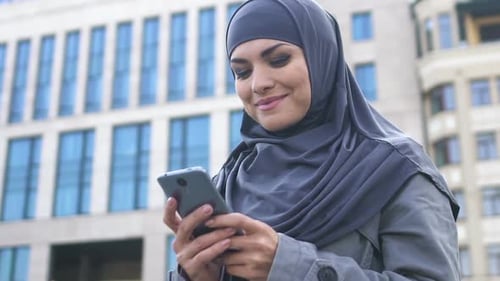 Woman in Headscarf Using Mobile Phone in City