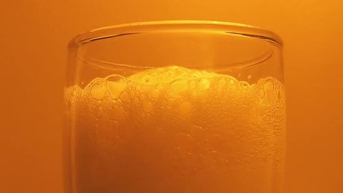 Nahaufnahme von Bierschaum im Glas vor orangefarbenem Hintergrund. Statische