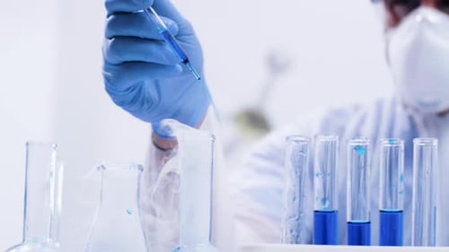 Nahaufnahme von Handaufnahmen eines Chemikers, der Lösung mit Pipette in eine reaktive blaue Flüssigkeit gießt
