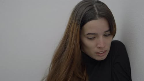 Closeup of Young Woman Sitting By Wall with Terrified Expression