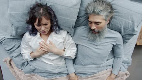 Une femme malheureuse se couvrant la tête avec un oreiller écoutant son mari ronfler dormir au lit ensemble