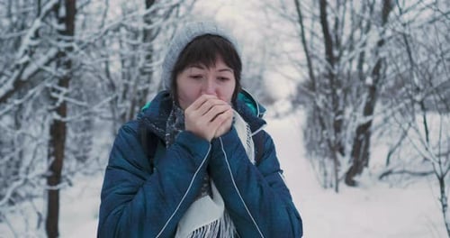 Frau wärmt ihre kalten Hände mit Atemspaß im verschneiten Winterwald