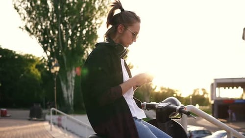 Young Adult on Scooter Using Mobile Phone at Sunset