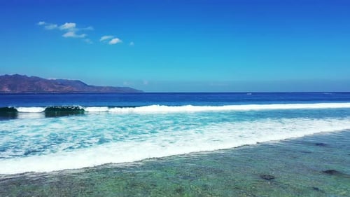 The White Waves Of The Deep Blue Ocean Splashes Towards The Seashore Background With High Mountains