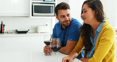 Couple interacting with each other while having glasses of red wine in the kitchen