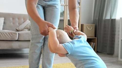 Toddler Making First Steps with Help of Mom
