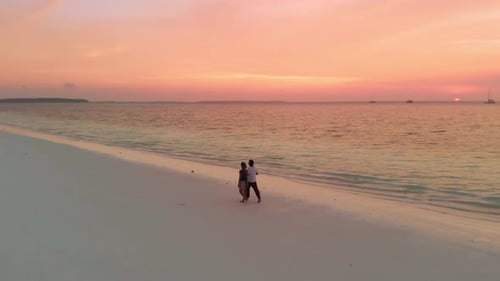 Couple on vacation walking on exotic beach with romantic dramatic sky at sunset