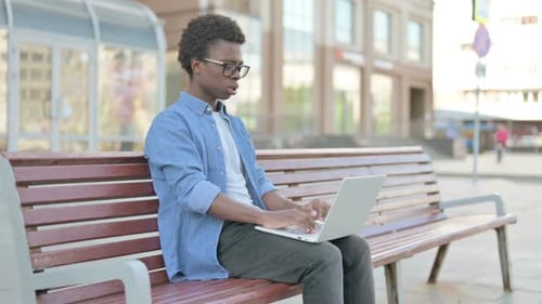 Young Man Using Laptop on City Bench