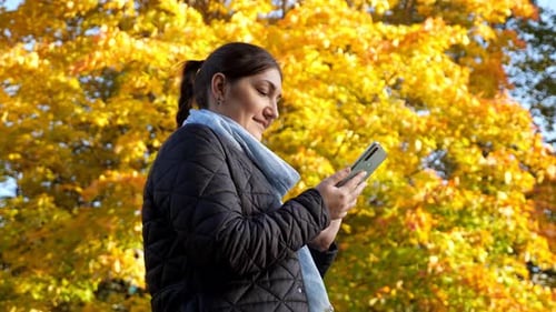 Woman Using Phone in Park in Autumn
