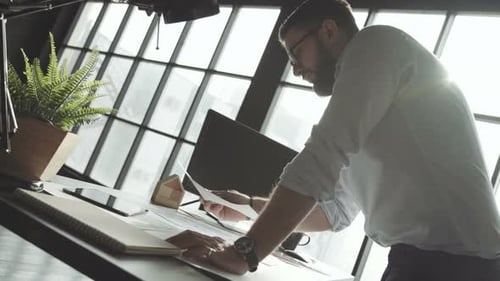 Young Businessman with a Beard Works Alone in Bright Spacious Office