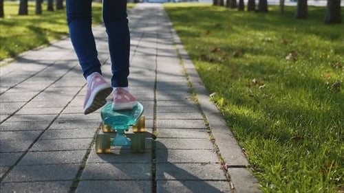 Dynamic video of legs of girl in jeans riding skateboard, steadicam, back view.