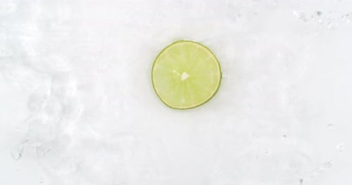 On a White Background Cut Into Slices of Lime Sprinkled with Water Spray. Juicy Fresh Lime in Slow