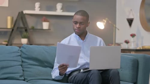 Man Working with Laptop and Paper on Sofa