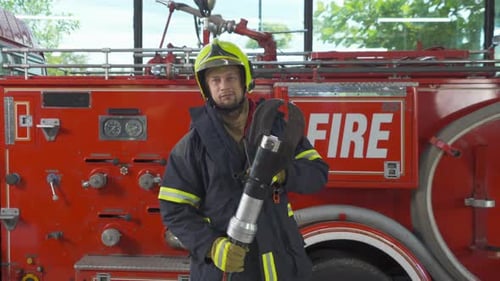 Firefighter Stands with Tool in Front of Firetruck