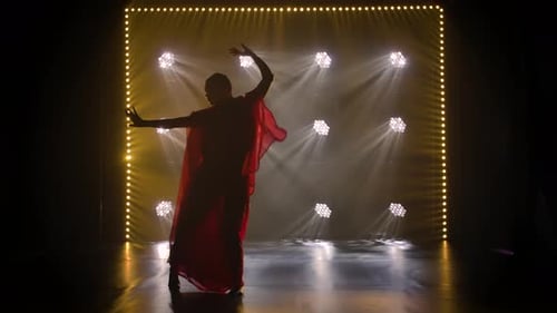 Silhouette d'une jeune fille danseuse dans un sari rouge, danse folklorique indienne, photographiée dans un studio sombre avec de la fumée