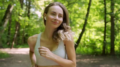 Athletic Young Woman with Headphones Listening To Music and Running in the Park