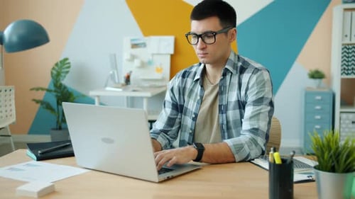 Slow Motion of Serious Man in Glasses Working with Laptop in Office Alone Typing Busy with Work
