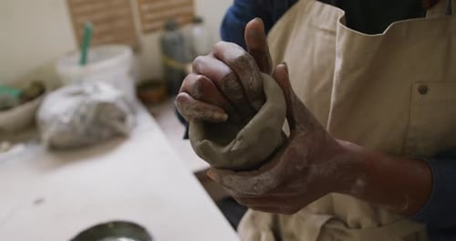 Mid section of female potter wearing apron working on clay to create pot at pottery studio