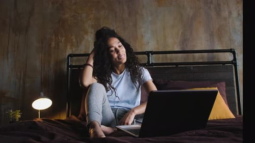 Junge attraktive afroamerikanische Frau nutzt Laptop für einen Videoanruf im Bett winkend