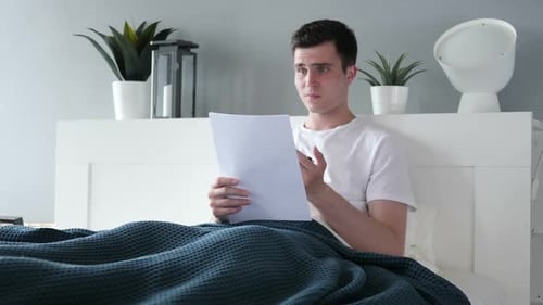 Young Adult Reads Paper in Bed Confused
